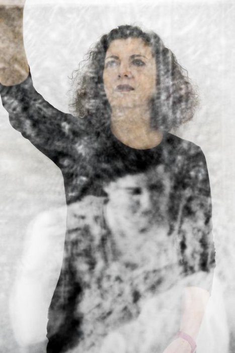 Mona Hatoum by Andri Pol 2013 Photograph of the artist with her arm raised with a projected image of a female portrait on her