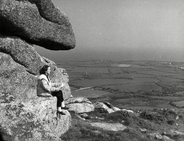 Barbara Hepworth sitting on large rocks looking out at fields below