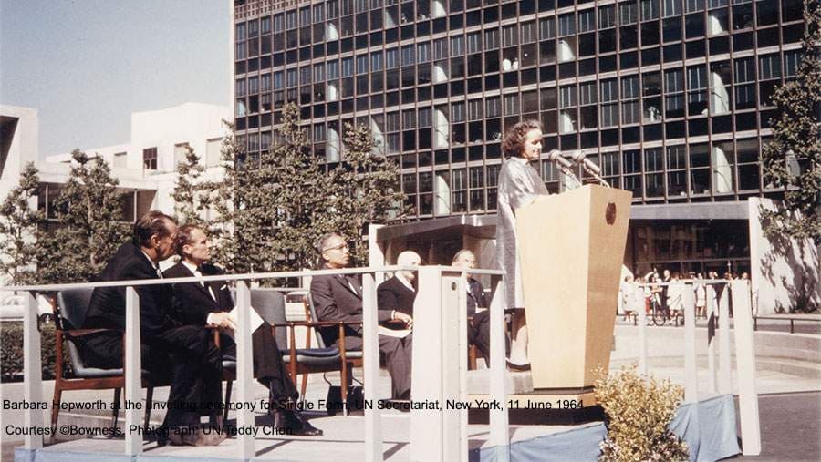 Barbara Hepworth speaking at a podium with men in suits sitting behind her