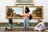 a parent or guardian stands in Tate Britain next to two children who are both looking at some paper resources
