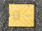 Square yellow electrical or gas plastic flap on the road surrounded by tarmac