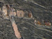 Micrograph of the area around the mask-like face of the left figure, below the mouth in the black area, showing pink, brown and black paint beneath