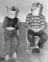 KwieKulik Activities with the Head 3 Parts still of a performance with two seated figures with buckets over their heads