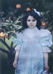 Vintage photograph of a young girl in a pale dress standing in front of an orange tree