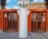 Entrance to Tate Liverpool. Two revolving glass doors with a bright orange frame. There is a pillar in front of the doors