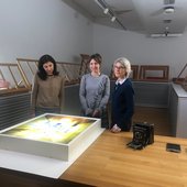 Three people pose looking at the camera. In front of them is a large photographic print on a lightbox.