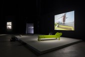 A green sofa on a platform in front of a screen in an empty gallery