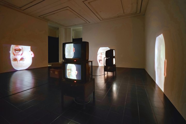 A room with TV monitor on the floor and projections of a man's face